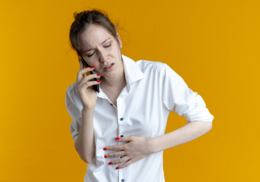 young aching blonde russian girl puts hand on belly talking on phone isolated on orange background with copy space.
Кишечные инфекции