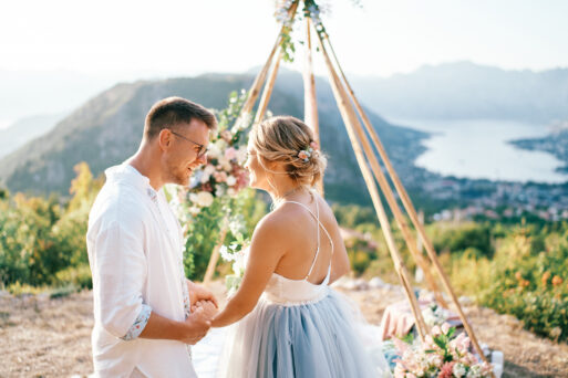 Laughing bride and groom hold hands while looking at each other at a tipi wedding arch on a mountain above the Bay of Kotor. Montenegro. High quality photo
свадьба