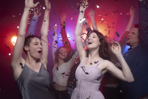 Девушки зодиака Близнецы радостно танцуют на вечеринке в июле месяце. Горят цветные огни и сверху сыпятся блестки