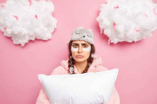 Puzzled worried woman has two pigtails awakes after seeing nightmare holds soft pillow applies beauty patches under eyes wears pajama and sleepmask poses against pink background white clouds above
Сны