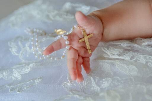 Child's hand with a crucifix on a white cloth.
Крестины