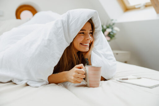 Woman smiles in bed, holding coffee cup with sleeve, happy
Кофе в постель