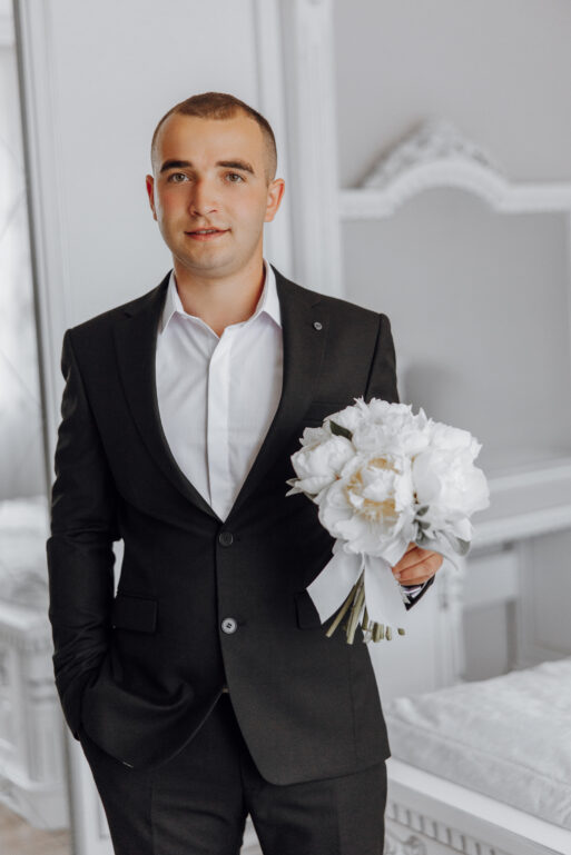 A man in a suit holding a bouquet of white flowers. Concept of elegance and sophistication, as the man is dressed in a formal suit and holding a beautiful bouquet of flowers